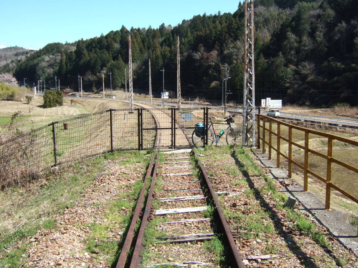 Looking down a derelict narrow-gauge railroad track that passes through a closed gate several meters away. A bicycle is parked at the gate.