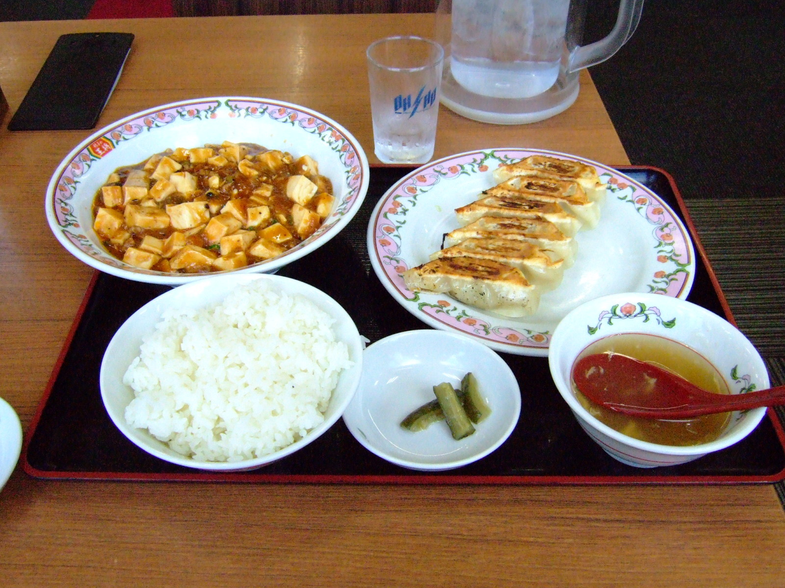 A restaurant meal of mabo-dofu, gyoza, white rice, salt pickles, and egg soup.