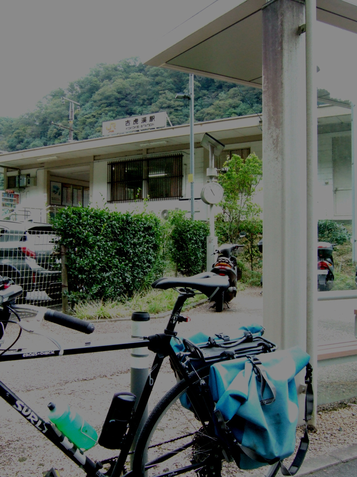 A blurry photograph of a bicycle parked in front of a rural train stop.