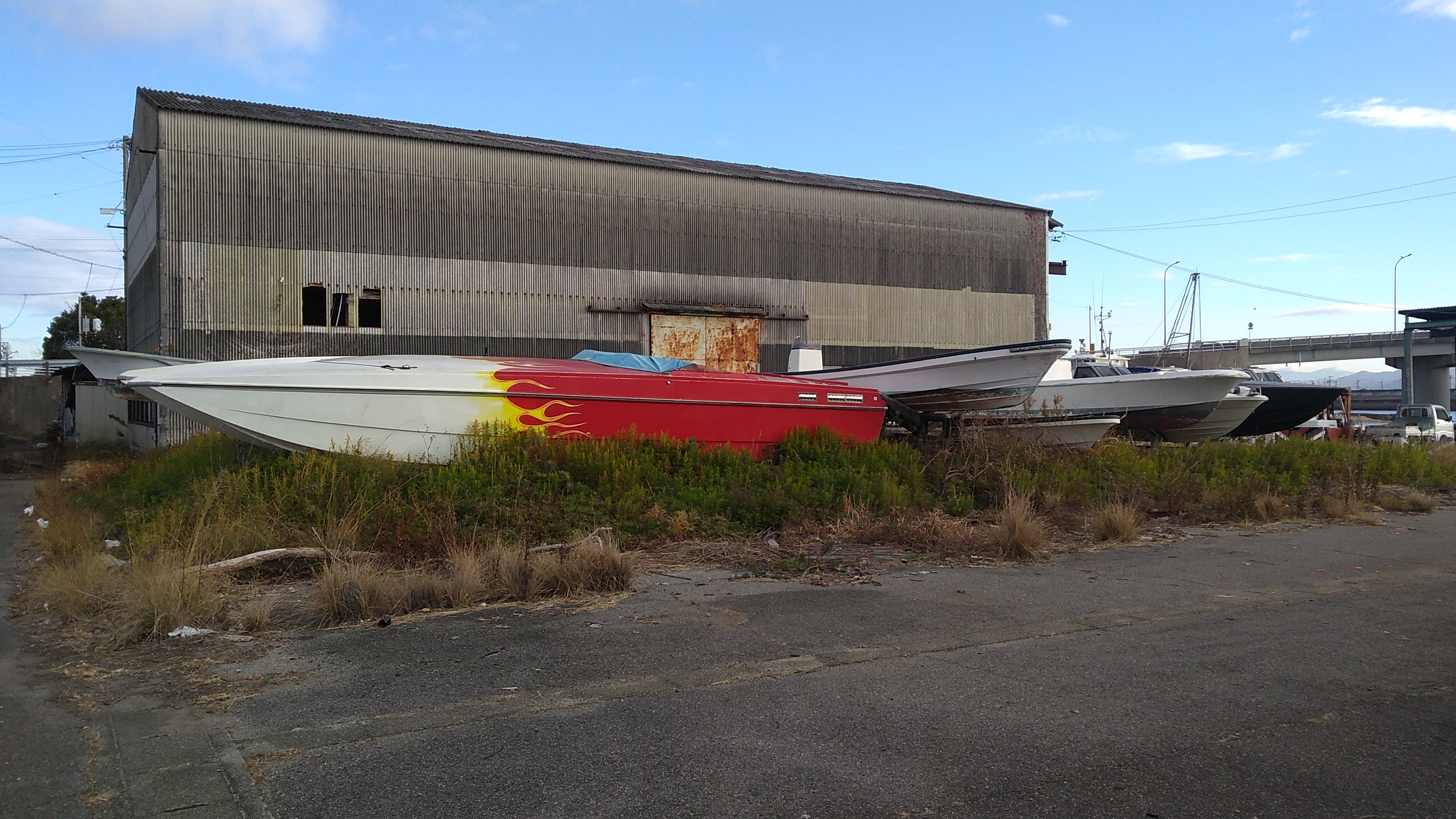 A long motorboat decorated with a flame motif, standing in a parking lot.