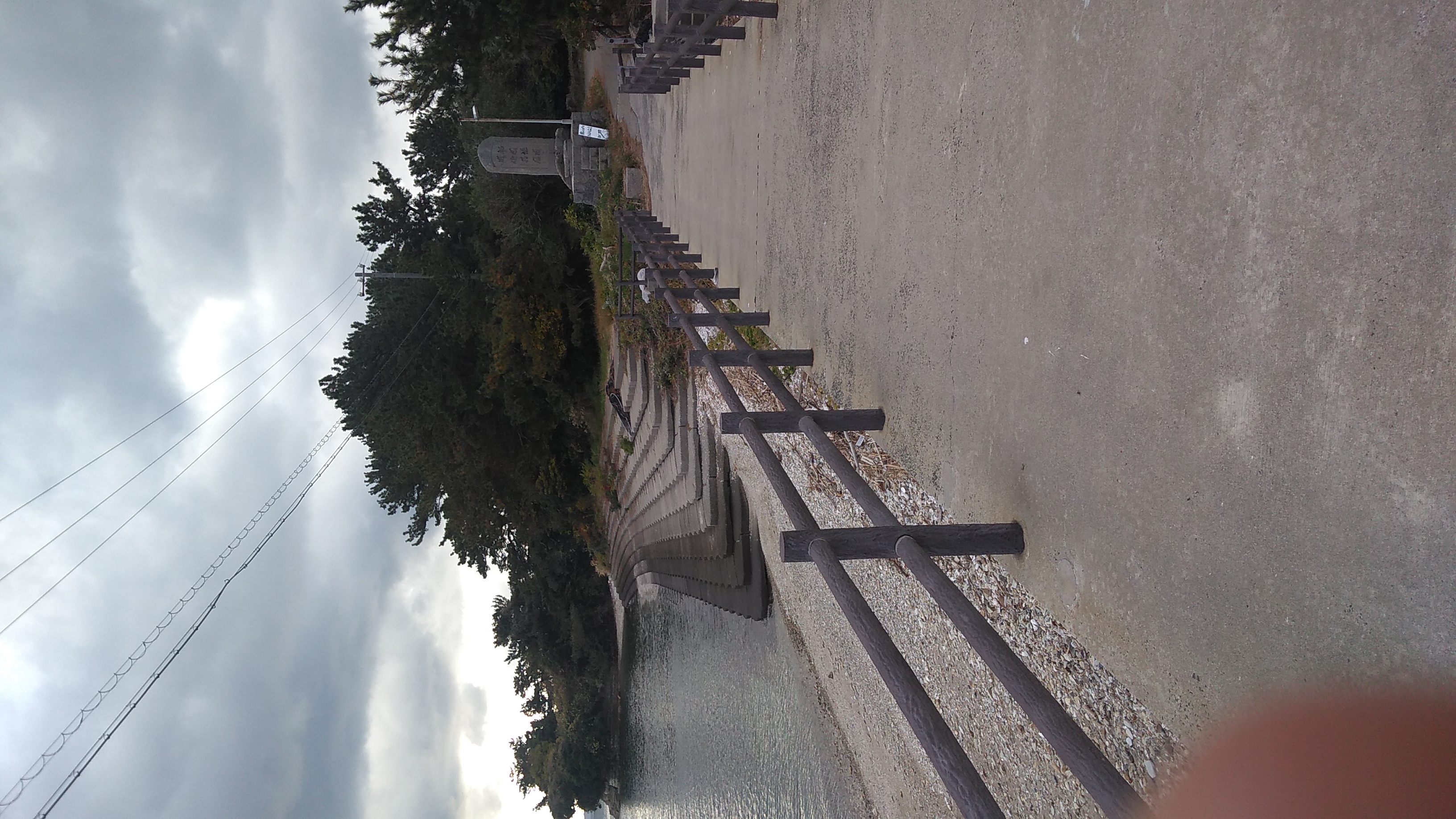 A concreted path with handrails running over a causeway leading to a small island. A stela too distant for the text to be legible stands at the end of the causeway.