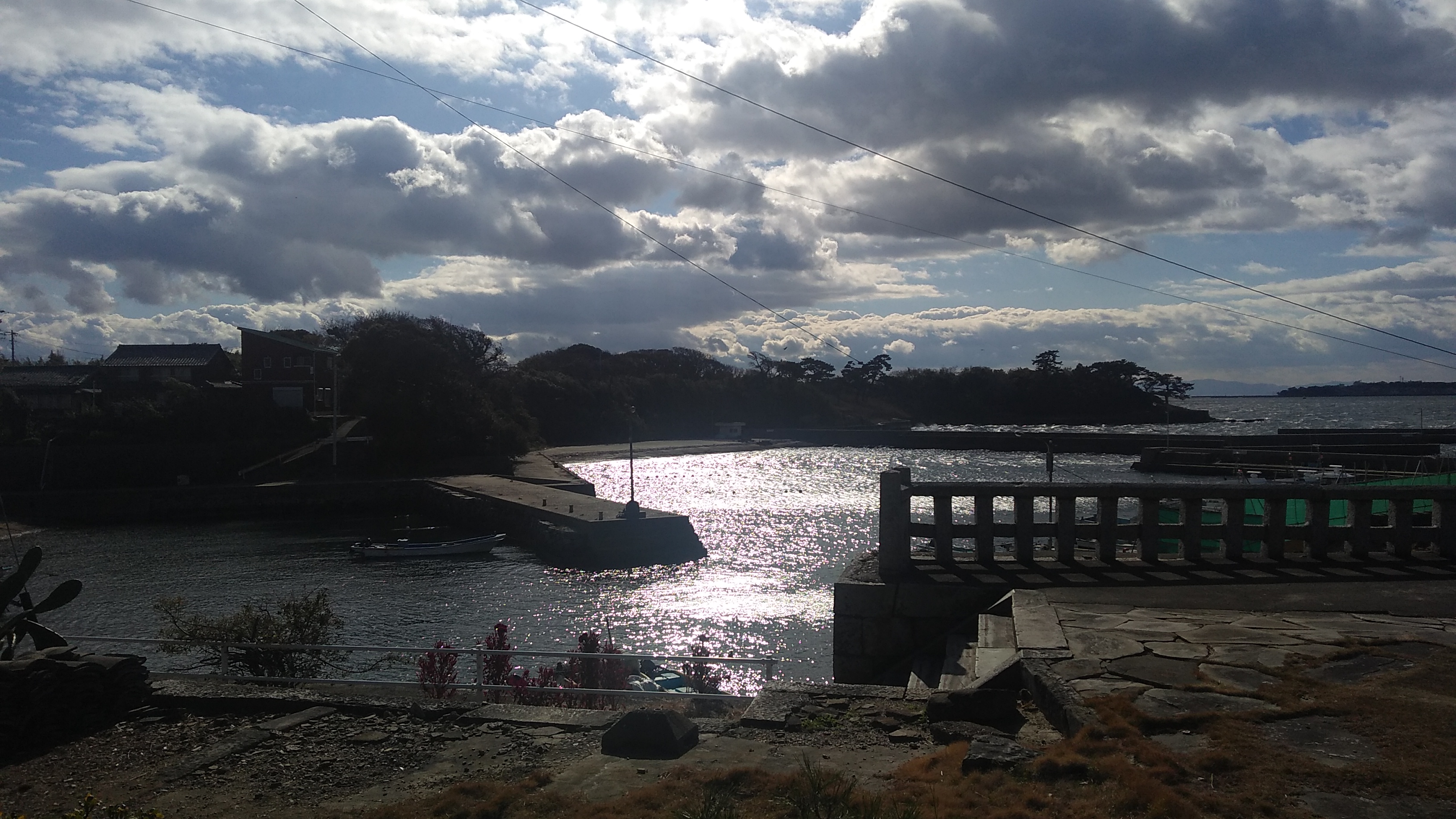 Cumulus clouds lit from behind over a coastal inlet, the sun reflecting brightly off the water, and the land darkened in shadow.