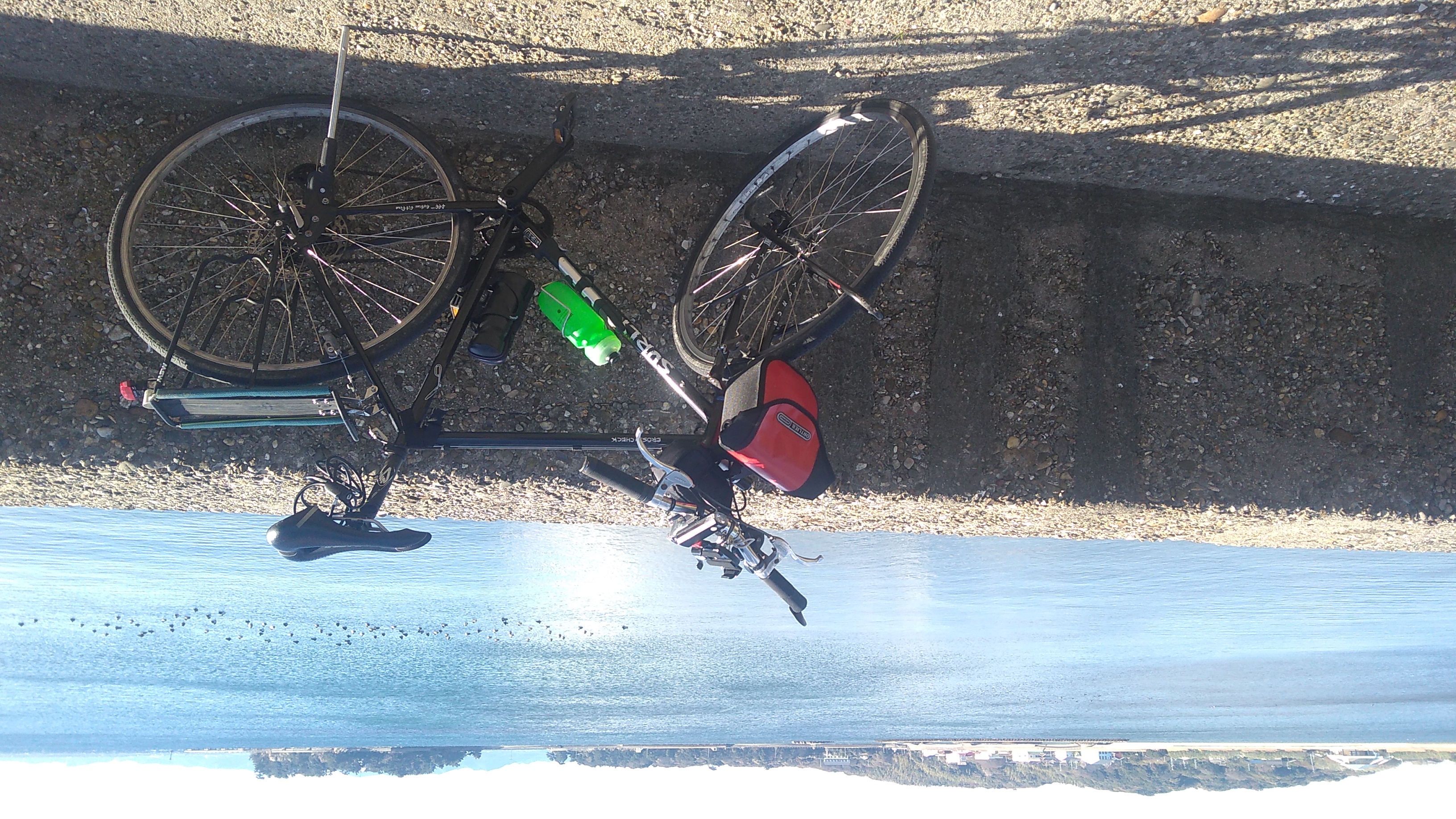 A bicycle parked at a low wall overlooking blue lagoon bounded by low-lying forested land in the distance.