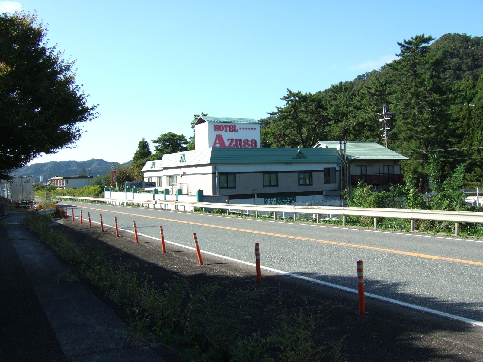 A building with rather faded paint at the side of a highway, with a sign rising above reading “Hotel Azusa”.