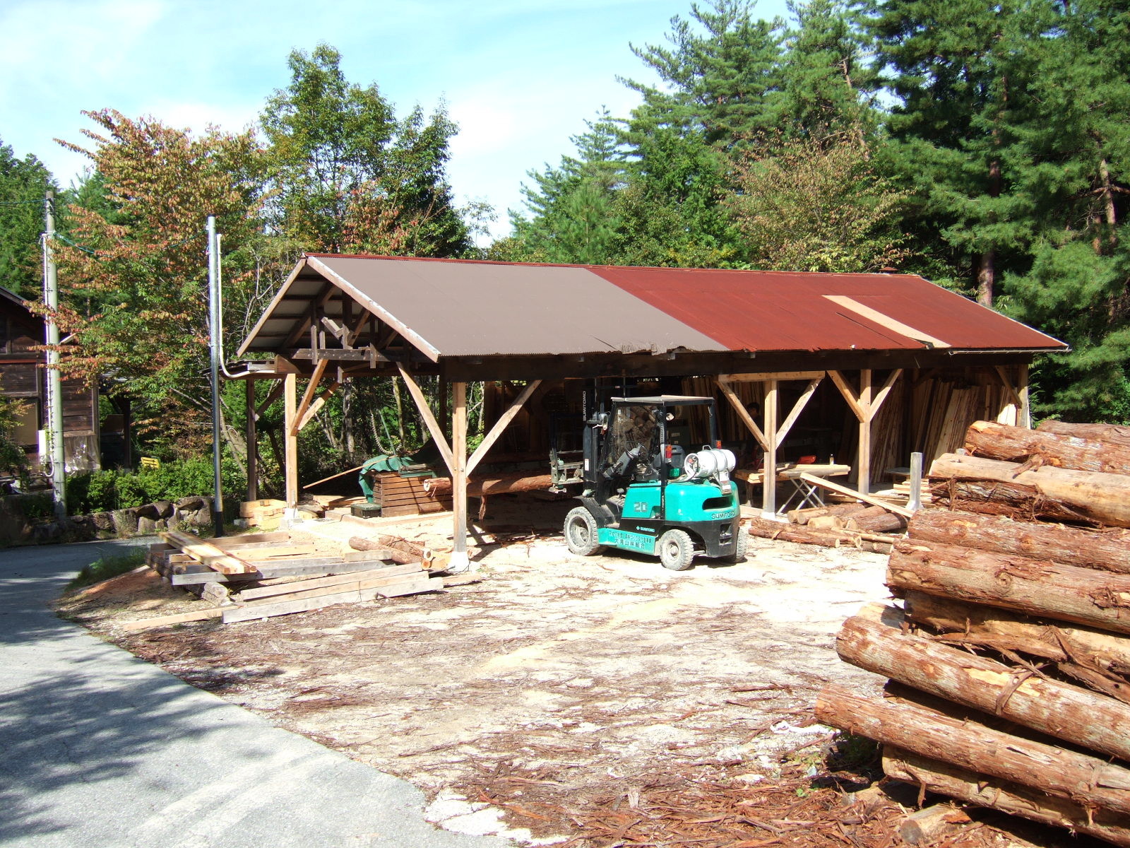 A peaked roof building with open sides covers a sawmill. A forklift is parked in front of the building.